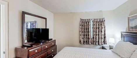 Um quarto com cama, cômoda, televisão e cortinas.