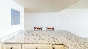 A kitchen with a granite countertop, two chairs, and a blue cabinet. - Water's Edge Resort 1002 (Murrells Inlet)