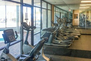 Varias bicicletas estáticas alineadas en un gimnasio con amplios ventanales y un panel de control.
