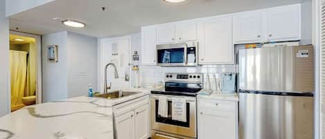 A modern kitchen with white cabinets, stainless steel appliances, and a wooden floor.