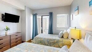 A hotel room with two beds, a TV mounted on the wall, a desk with drawers, a chair, and a window with curtains. - Ocean View Escape Retreat (Myrtle Beach)