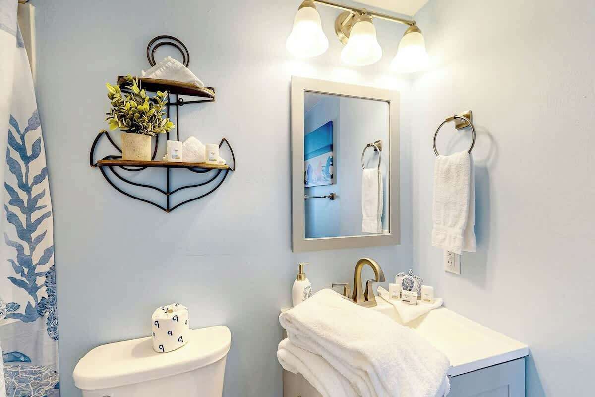 A bathroom with a toilet, sink, towel rack, and a shelf with a plant.
