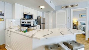 A modern kitchen with white cabinetry, a marble island, and a 'WELCOME' sign. - Ocean View Escape Retreat (Myrtle Beach)