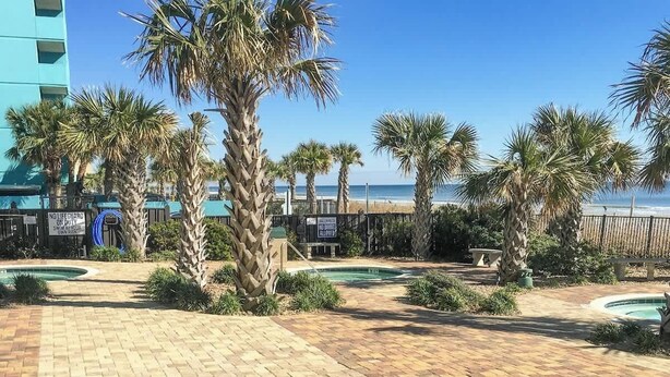 A pool area with palm trees and a beach view. - Ocean View Escape Retreat (Myrtle Beach)