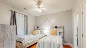 A bedroom with two beds, a ceiling fan, a window with blinds, and a wall-mounted light fixture. - Seas the Day at Magnolia Place (Myrtle Beach)