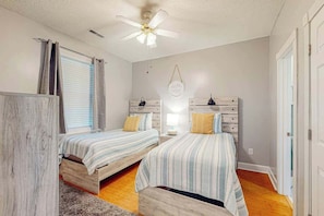 A bedroom with two beds, a ceiling fan, a window with blinds, and a wall-mounted light fixture. - Seas the Day at Magnolia Place (Myrtle Beach)
