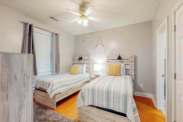 Ein Schlafzimmer mit zwei Betten, einem Deckenventilator, einem Fenster mit Jalousien und einer Wandleuchte.
