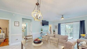A spacious living room with a dining area, a ceiling fan, and a large window with curtains. - Seas the Day at Magnolia Place (Myrtle Beach)