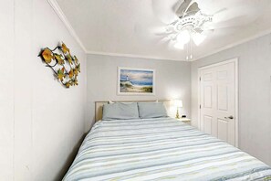 A bedroom with a bed, a painting, a decorative wall piece, and a door. - Ocean Forest Villas E-308 (Myrtle Beach)