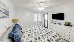 A bedroom with a bed, a ceiling fan, a TV, a dresser, and a window with blinds. - Ocean Forest Villas E-308 (Myrtle Beach)