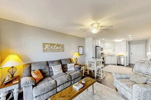 A living room with a grey sofa, a wooden coffee table, and a kitchen in the background. - Ocean Forest Villas E-308 (Myrtle Beach)