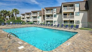 A rectangular swimming pool with a tiled deck, surrounded by lounge chairs and a multi-story building with balconies. - Ocean Forest Villas E-308 (Myrtle Beach)