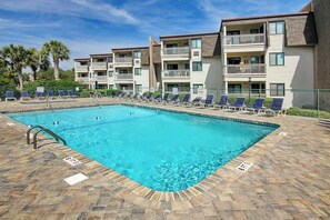 A rectangular swimming pool with a tiled deck, surrounded by lounge chairs and a multi-story building with balconies. - Ocean Forest Villas E-308 (Myrtle Beach)