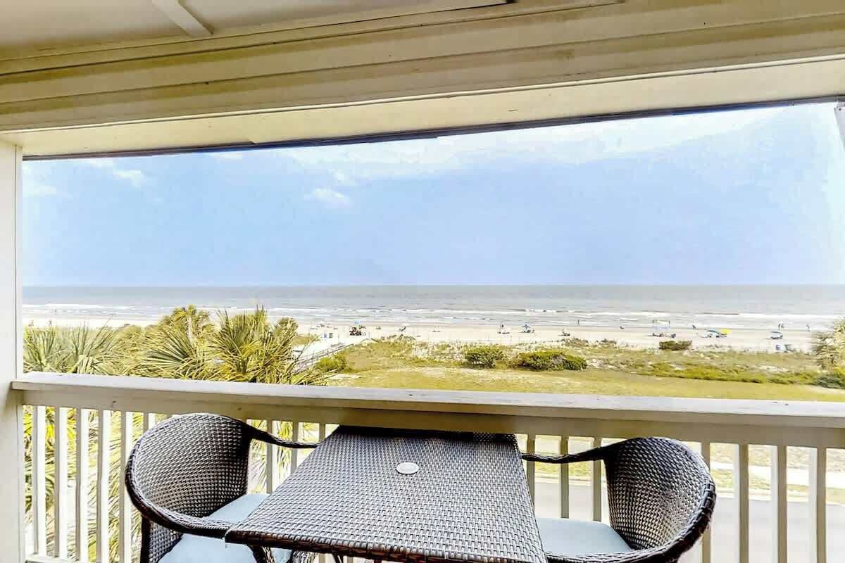 Un balcón con vista a la playa, una mesa y dos sillas.