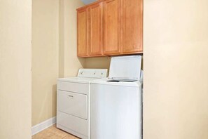 A laundry area with a washing machine and dryer, wooden cabinets above, and a light-colored floor. - Tuscan Ocean Vista, Unit D (Myrtle Beach)