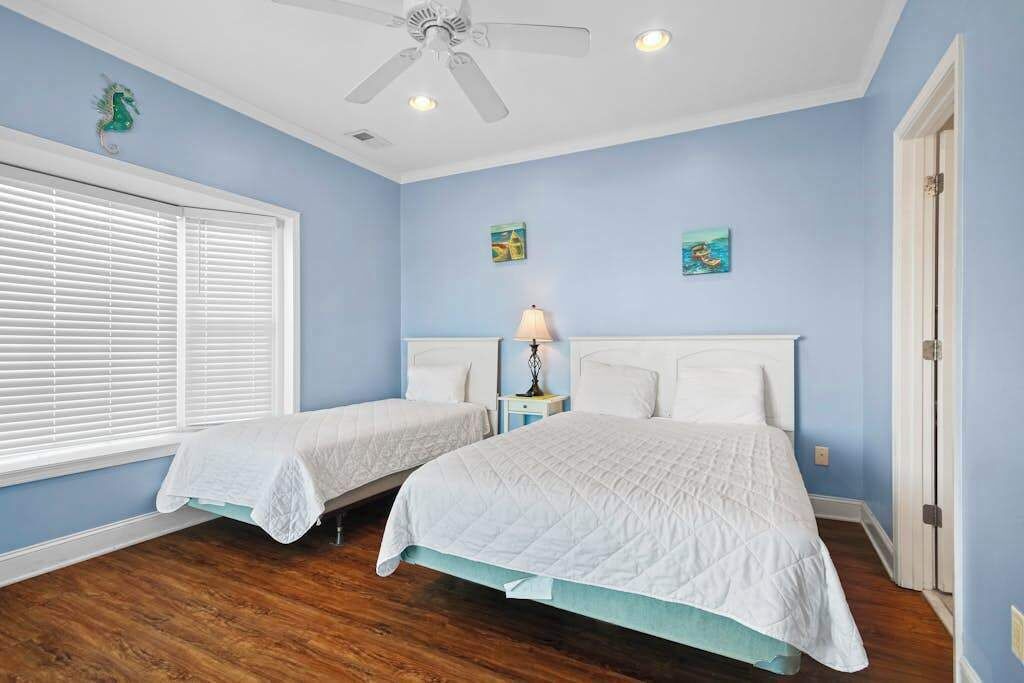 A bedroom with two beds, a ceiling fan, and artwork on the walls.