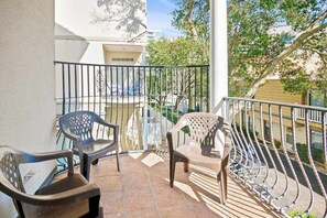 A balcony with two plastic chairs, a metal railing, and a view of a building and trees. - Tuscan Ocean Vista, Unit D (Myrtle Beach)