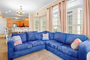 A living room with a blue sectional sofa, a dining table with chairs, and a kitchen in the background. - Tuscan Ocean Vista, Unit D (Myrtle Beach)
