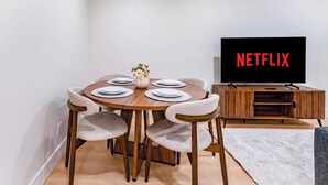 Ein Essbereich mit einem runden Tisch, Stühlen, einer Blumenvase und einem Fernseher, der 'NETFLIX' an der Wand zeigt.