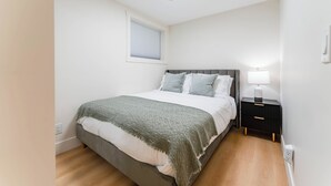 Ein Schlafzimmer mit Bett, Nachttisch, Lampe und einem Fenster mit Jalousien.
