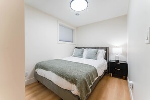 A bedroom with a bed, bedside table, lamp, and a window with blinds.