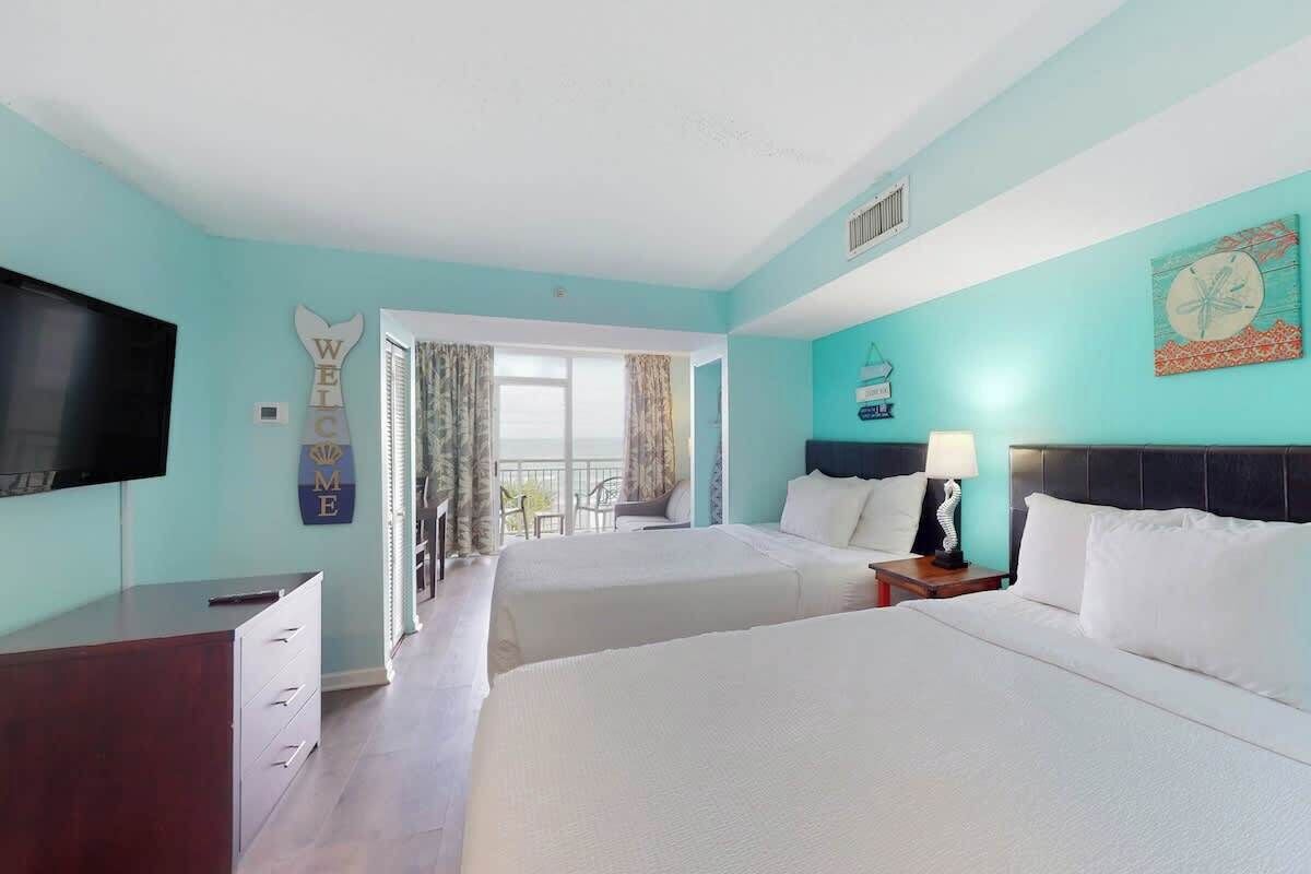 A hotel room with two beds, a TV, a desk, and a balcony.