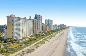 A beachfront hotel with multiple high-rise buildings, a sandy beach, and a clear view of the ocean. - Camelot by the Sea 0303 (Myrtle Beach)