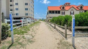 Ein Weg, der zu einem Gebäude mit rotem Dach führt, gesäumt von einem Zaun und einem Schild, das einen öffentlichen Fußweg kennzeichnet.
