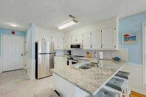 A modern kitchen with white cabinets, stainless steel appliances, a granite countertop, and a built-in sink. - Emerald Pointe Unit 1-C (North Myrtle Beach)