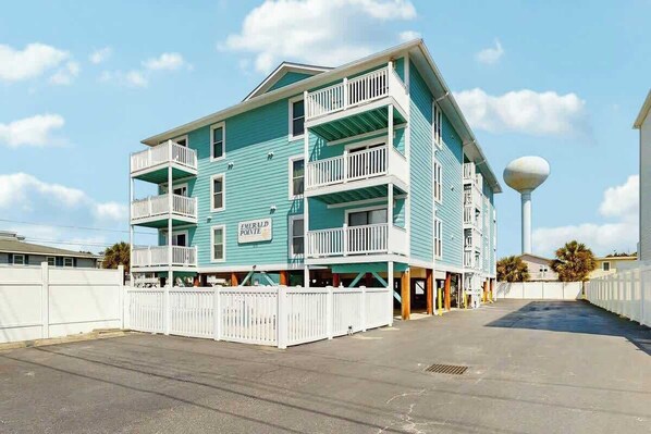 A multi-story building with balconies, a sign indicating 'Emerald Pointe,' and a clear sky. - Emerald Pointe Unit 1-C (North Myrtle Beach)