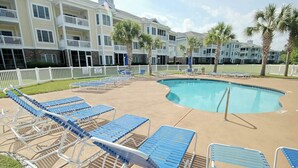 Une zone avec une piscine, des chaises longues et un bâtiment doté de balcons en arrière-plan.