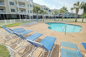 A pool area with lounge chairs and a building with balconies in the background. - Magnolia Escape Retreat (Myrtle Beach)