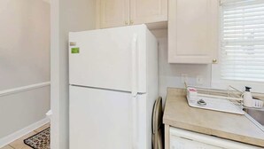 Une cuisine avec des meubles blancs, un réfrigérateur blanc et un plan de travail sur lequel se trouvent une bouilloire et une machine à café.