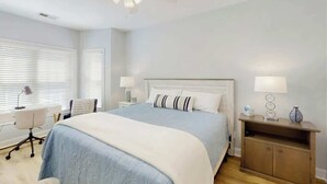 Une chambre à coucher comprenant un lit, des tables de chevet, un bureau et un ventilateur de plafond.