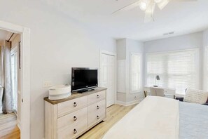 Ein Schlafzimmer mit einem Bett, einem Fernseher auf einer Kommode, einem Schreibtisch mit Stuhl und einem Fenster mit Jalousien.
