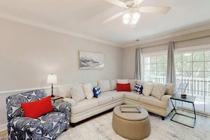 A living room with a sectional sofa, a patterned armchair, a round ottoman, a side table, and a ceiling fan. - Magnolia Escape Retreat (Myrtle Beach)