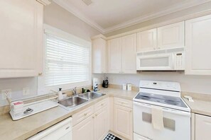 A kitchen with white cabinets, a microwave, a stove, a sink, and a window with blinds. - Magnolia Escape Retreat (Myrtle Beach)