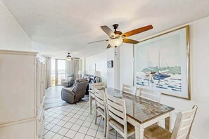 A dining area with a table and chairs, a ceiling fan, and a painting of boats on the wall. - The Summit Unit 2-A Condo (North Myrtle Beach)