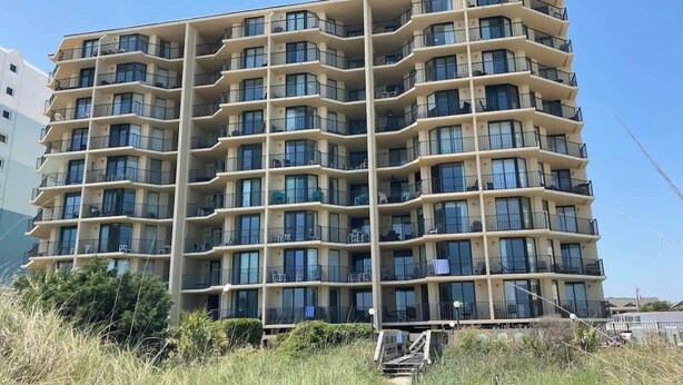 A multi-story hotel with balconies, a clear sky, and a pathway leading to the entrance. - The Summit Unit 2-A Condo (North Myrtle Beach)