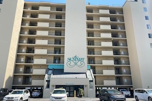A multi-story hotel with a prominent logo, balconies, and a parking area. - The Summit Unit 2-A Condo (North Myrtle Beach)
