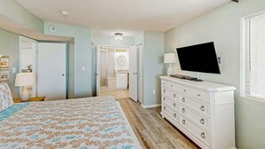 A bedroom with a bed, dresser, TV, and a bathroom visible through an open door. - The Summit Unit 2-A Condo (North Myrtle Beach)