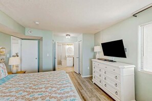 A bedroom with a bed, dresser, TV, and a bathroom visible through an open door. - The Summit Unit 2-A Condo (North Myrtle Beach)