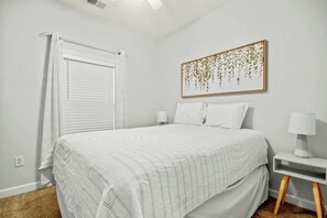 A bedroom with a bed, a nightstand, a lamp, a window with blinds, and a wall-mounted picture. - Cypress Bend Unit 222 (North Myrtle Beach)