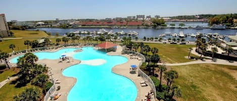 A large outdoor swimming pool with a wavy design, surrounded by palm trees and lounge chairs.