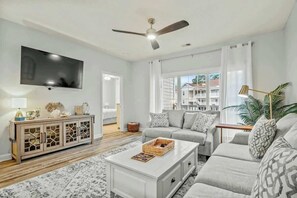 Ein Wohnzimmer mit Flachbildfernseher, Deckenventilator, Sofagarnitur, Couchtisch und einer Schranke mit Glastüren.