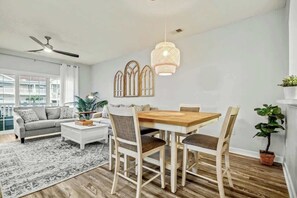 Ein modernes Wohnzimmer mit einem Holzesstisch, weißen Stühlen, einem grauen Sofa und einem Deckenventilator.