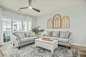A living room with two grey sofas, a white coffee table, patterned rug, and decorative wooden window shades. - Cypress Bend Unit 222 (North Myrtle Beach)