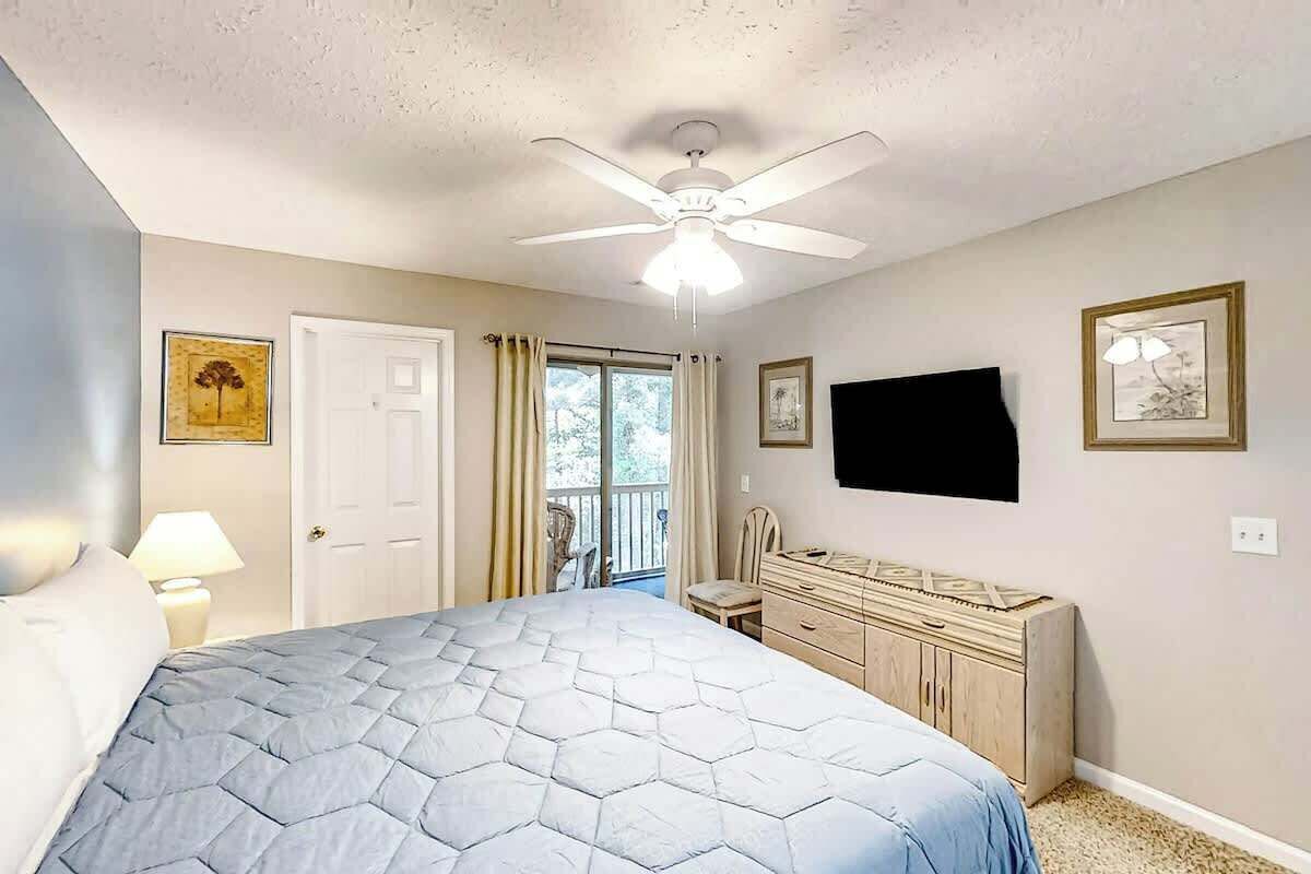 Ein Schlafzimmer mit einem Bett, einem Deckenventilator, einem Schminktisch, einem Fernseher und einer Tür.
