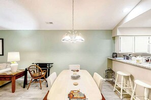 A dining area with a table, chairs, a chandelier, and a kitchen area with cabinets and a countertop. - Pinehurst Condos Unit 6J (Pawleys Island)