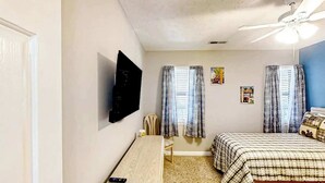 Un dormitorio con cama, escritorio, silla, televisor y ventilador de techo.
